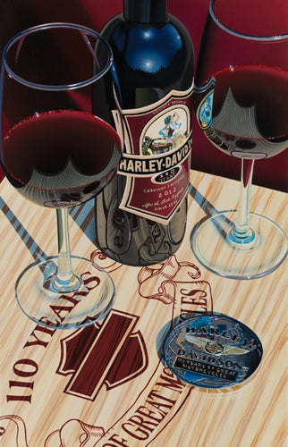 Red wall background, wooden table with the Harley-Davidson logo and "110 Years". Two glasses of red wine and a bottle of Harley Davidson wine with a coin.