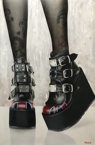 A woman's legs are pictured from the calves down. Behind some dark translucent tights are multiple tattoos, from a face of Elvis to a red anarchy emblem. She is wearing black platform heels with several metal buckles and a red pattern on the toe, all on a white and gray background.