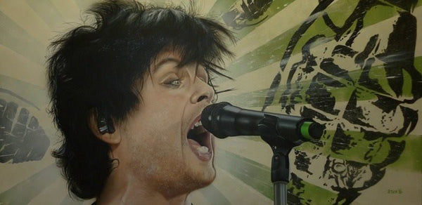 Billie Joel Armstrong of Green Day is pictured from the neck up, expressively singing into a microphone on a stand. A green and white striped background is printed with several black grenades. 