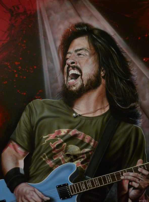 Dave Grohl from Foo Fighter is pictured from the hips up, slightly angled left. He is wearing a green and red shirt with skulls and crossbones on it, and is holding a blue electric guitar. He's got a wide, open mouthed smile on his face. In the background is a red and black splash with a white spotlight.